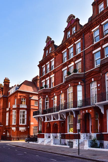 A detailed exterior view of the Royal College of Music building in Kensington, featuring red brick and stone architectural elements, large arched windows, decorative spires, and intricate stone carvin